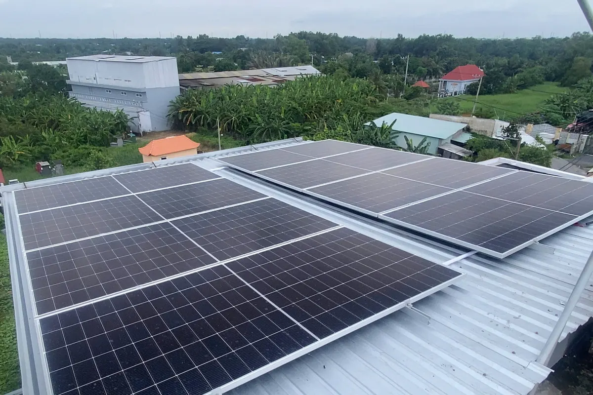 Hai cụm tấm pin trên ray nhôm và chân đế bắt sóng mái tôn, phía xa là vườn chuối và nhà dân