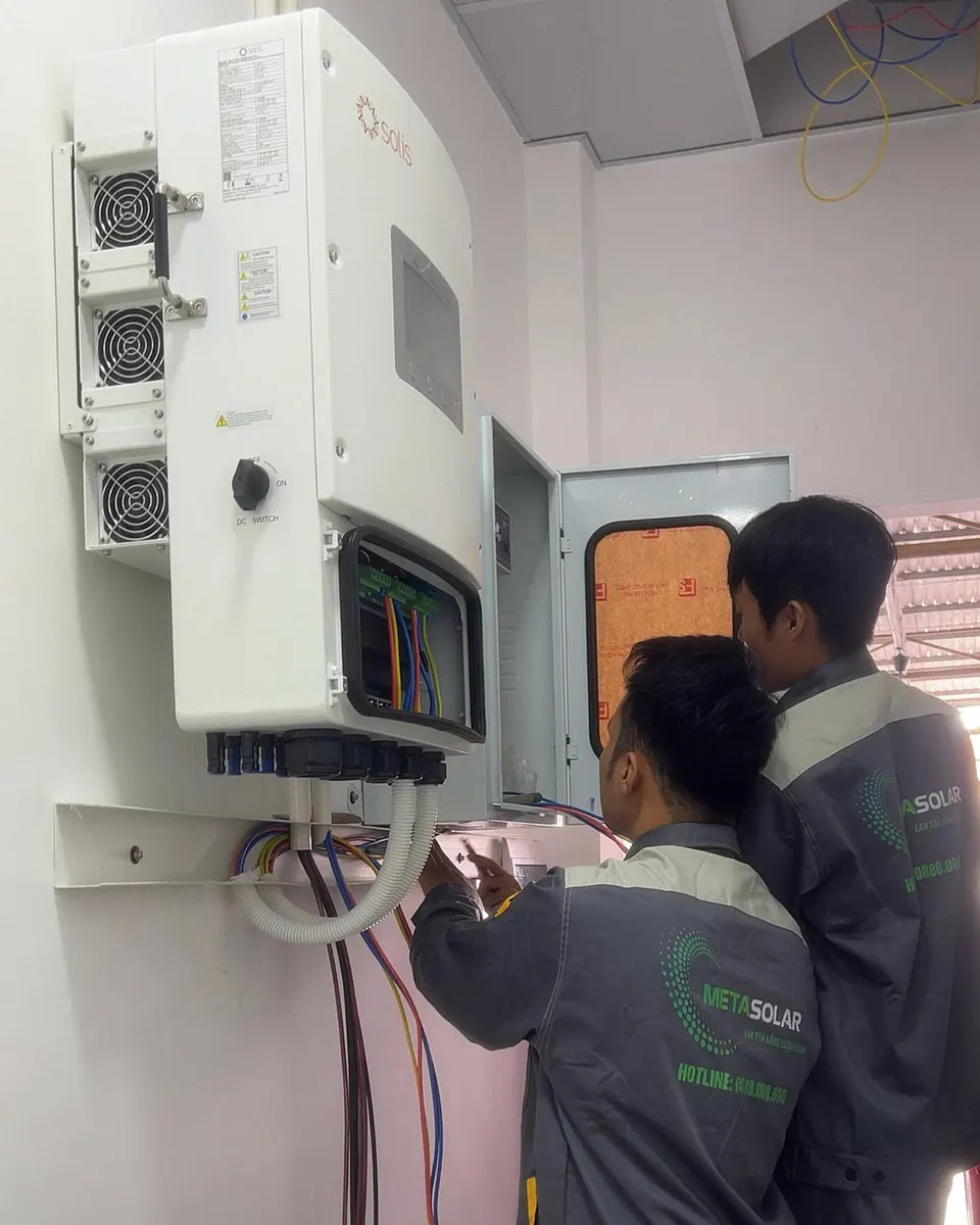 Hai kỹ thuật viên đấu dây AC vào hộp đấu nối đã mở nắp của inverter gắn tường