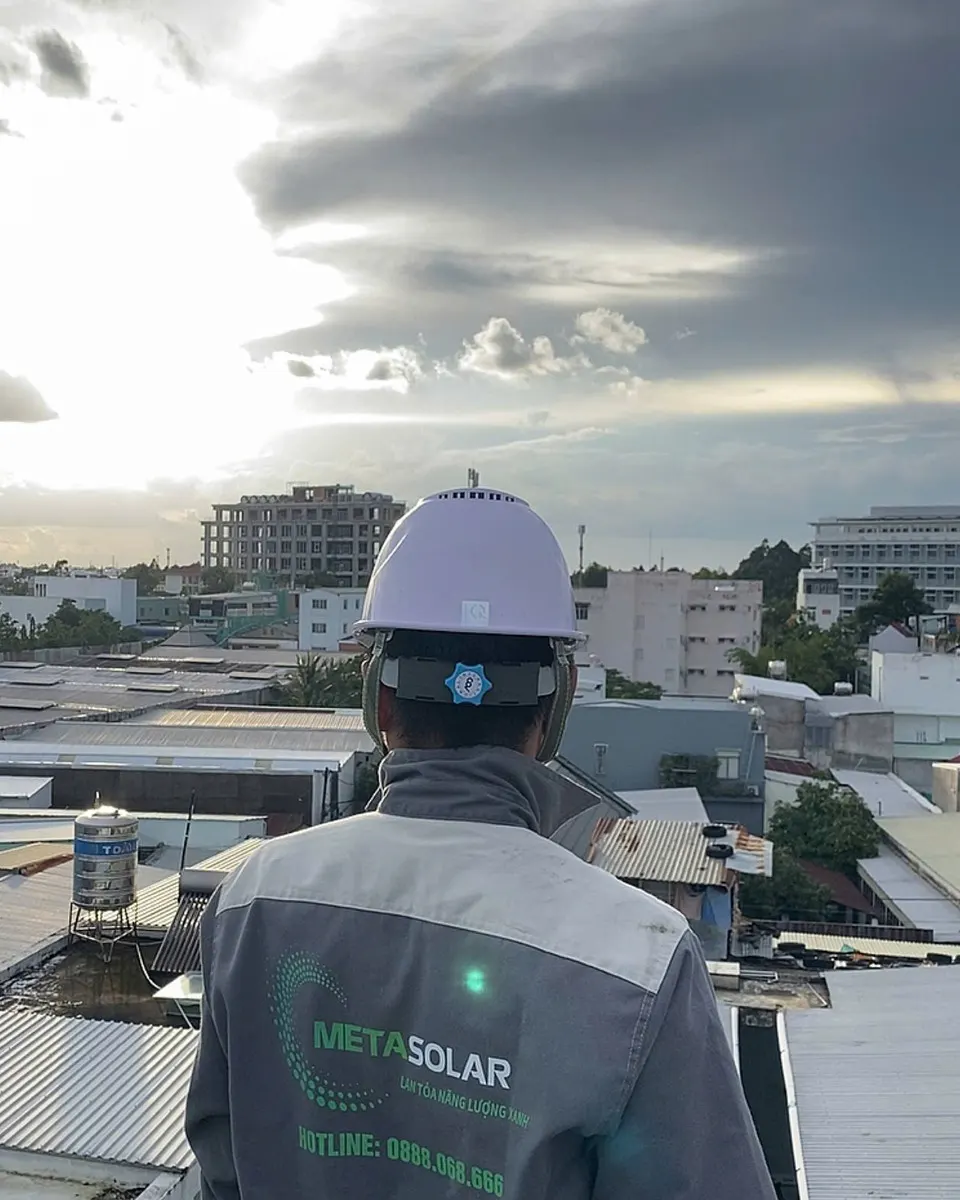 Kỹ thuật viên đội mũ bảo hộ đứng quay lưng nhìn ra một khu mái tôn đô thị trước khi khảo sát
