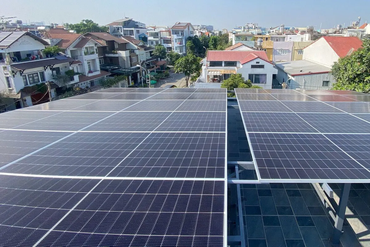 Hai mảng tấm pin trên khung thép làm mái che sân thượng lát gạch, nhìn ra dãy nhà phố mái ngói đỏ